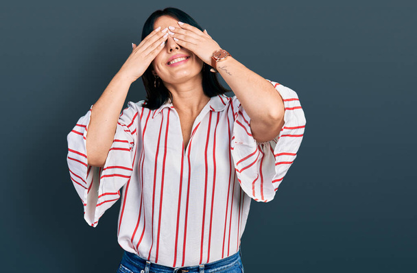 Jong Latijns-Amerikaans meisje draagt casual kleren die ogen bedekken met handen glimlachend vrolijk en grappig. blind concept.  - Foto, afbeelding