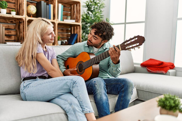 Hombre tocando la guitarra española a su novia sentada en el sofá en casa - Foto, imagen