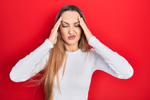 Junge blonde Mädchen in lässiger Kleidung leiden unter Kopfschmerzen verzweifelt und gestresst, weil Schmerzen und Migräne. Hände auf den Kopf.  - Foto, Bild