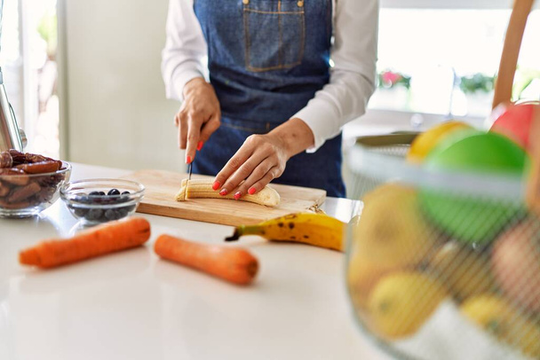 Young blonde woman cutting banana at kitchen - Foto, imagen