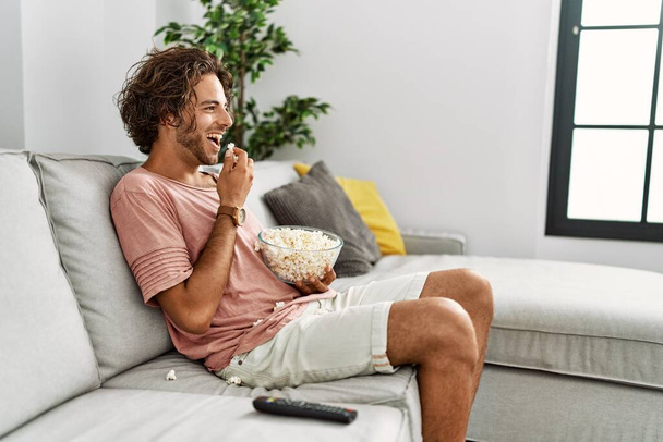 Jeune homme hispanique regardant un film assis sur le canapé à la maison. - Photo, image