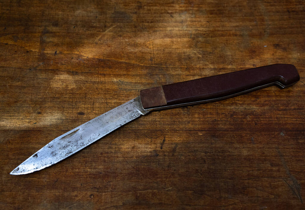 A large folding knife on a wooden table. Criminal showdowns on domestic grounds. - Fotó, kép