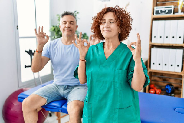 患者と痛みの回復クリニックで働く理学療法の女性はリラックスし、指で瞑想ジェスチャーを行う目を閉じて笑顔。ヨガのコンセプト.  - 写真・画像