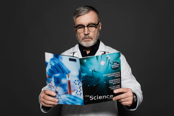 médico sênior em óculos de leitura revista científica isolado em cinza escuro - Foto, Imagem