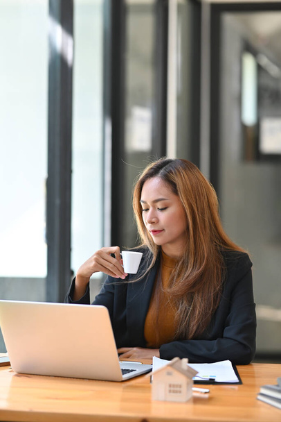 Portrait of confident businesswoman drinking coffee and working in modern office. - Photo, image
