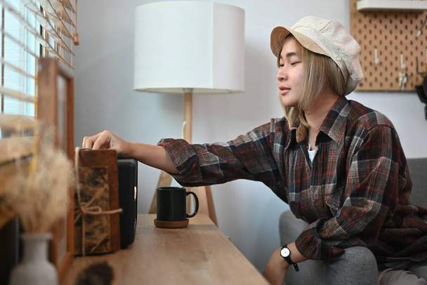リビングルームでワイヤレススピーカーをオンに幸せな若いアジアの女性. - 写真・画像