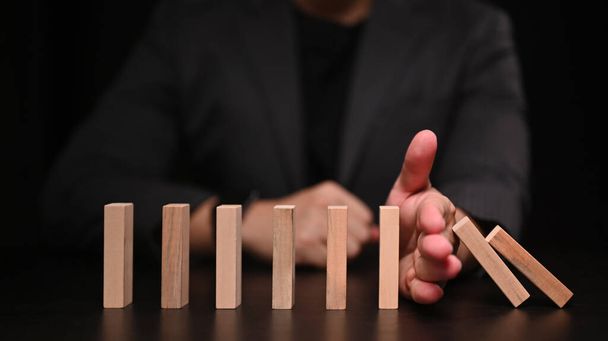 Podnikatelská ruka se snaží zastavit domino. Ochrana financování z domino efekt konceptu. - Fotografie, Obrázek