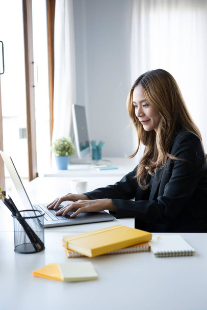 Charming businesswoman sitting in bright modern office and working with laptop. - Фото, зображення