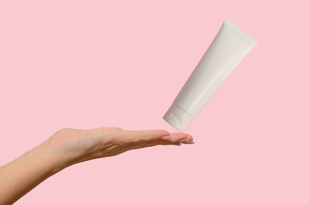 Hands hold a white container with cosmetic cream. For body care. On a pink background. - Foto, afbeelding