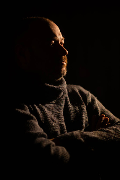 The man folded his hands in a sweater. Dark background, silhouette. Thoughtfulness, meditation, midlife crisis concept. A middle-aged man, forty years old. - Фото, изображение