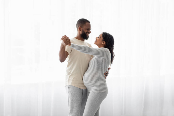 Satisfied cute young african american male and pregnant woman dance on window background, celebrate good news - Foto, Bild