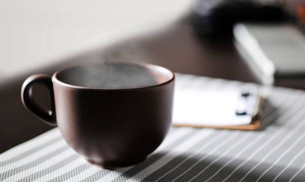 brown cup of coffee, with hot steam, on the work desk - Fotoğraf, Görsel