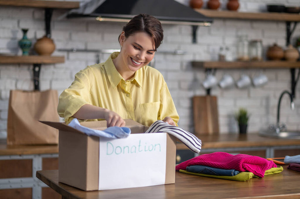 Cheerful young woman packing things for donation - Foto, immagini
