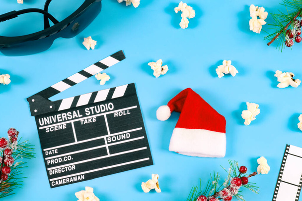 Movie clapperboard, popcorn, glasses, film strip, santa claus hat and spruce branches. - Fotó, kép