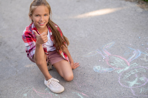 Pleased beautiful girl approving her chalk drawings on the ground - Foto, afbeelding