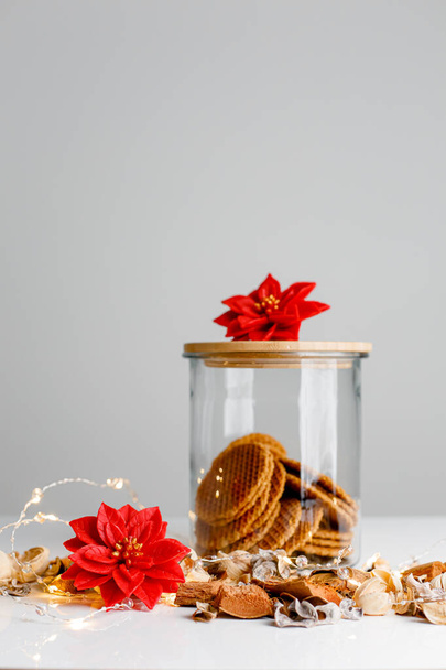 Rode poinsettia kaarsen op lichte kerstachtergrond met koekjes in glazen pot en houten potdeksel - Foto, afbeelding