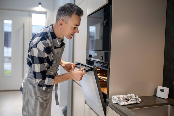 Man sideways to camera looking into open oven - Photo, image