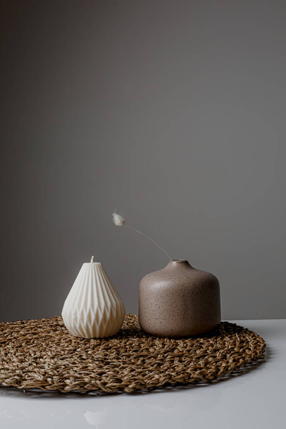 Cozy home interior decor, aromatic candles in glass glowingon white and grey background with natural oil, selective focus of fluffy bunny tail grass, brown jar, lotus flower candle, round matt ceramic - Fotografie, Obrázek