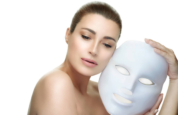 Güzel yüzlü, maskeli bir kadın. Foton terapisi hafif cilt yenileme yüz maskesi. Beyaz üzerine izole edilmiş yatay portre - Fotoğraf, Görsel