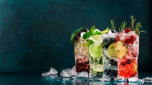 Cocktails or mocktails drinks. Classic summer refreshing long drink in highballs with berries, lime, herbs and ice on blue table background - Foto, Imagem