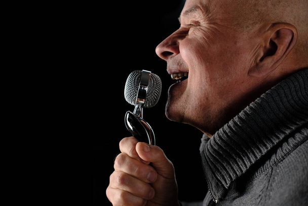 adult man emotionally screaming, singing into studio microphone on black background, music recording concept, blogger equipment - Фото, зображення