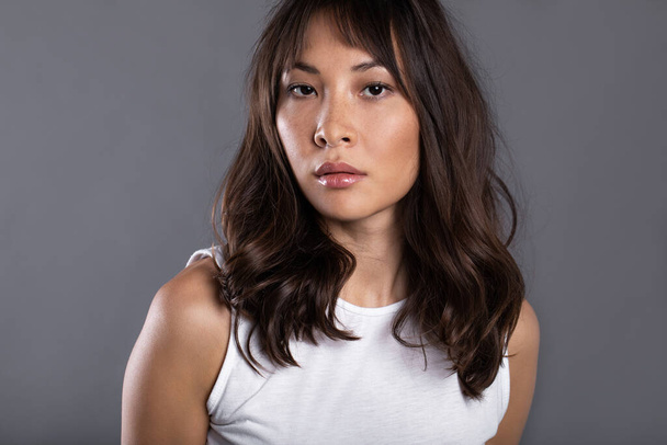Close-up portrait of Asian woman. Serious girl on gray background, studio shot. - Foto, Imagen