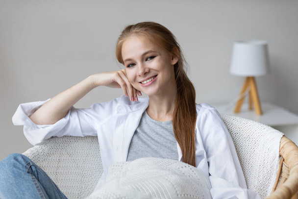 Close-up portrait of a cute happy smiling girl dreaming in a cozy armchair at home. Woman enjoy peaceful quiet lifestyle, stress free. - Foto, Bild