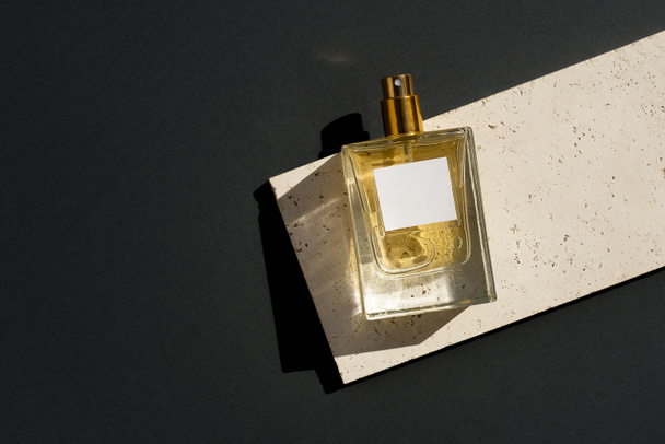 Transparante fles parfum met wit etiket op stenen plaat op een grijze ondergrond. Parfumpresentatie met daglicht. Trending concept in natuurlijke materialen. Essentie voor vrouwen en mannen. - Foto, afbeelding