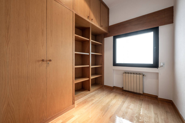 Empty room with built-in oak wardrobe and bookcase, oak parquet floor and aluminum radiator under the window - Fotó, kép