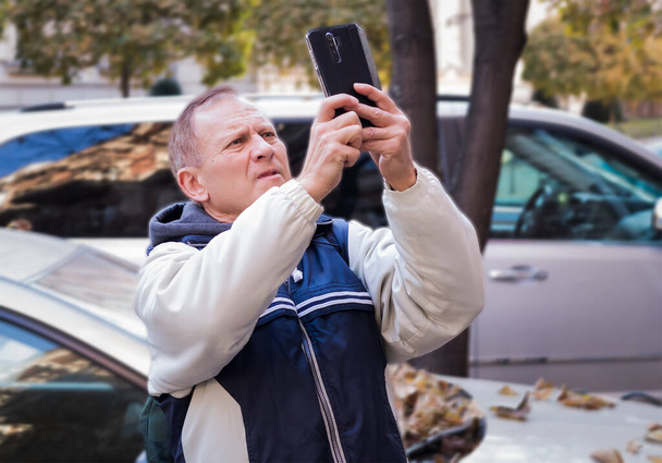 schöner Mann mittleren Alters steht neben dem Auto und hält ein Handy in der Hand - Foto, Bild