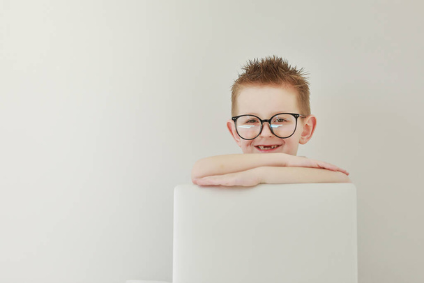 schoolboy in glasses using laptop sitting on bed. Child doing school homework and seriously and tired looking on camera.Online learning, distance lesson, education with online tutor at home isolation. - Фото, зображення