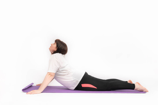 Junge Frau mit Übergewicht praktiziert Yoga. Mädchen versucht abzunehmen und treibt Sport auf Yogamatte. Seitenansicht. Weißer Hintergrund - Foto, Bild