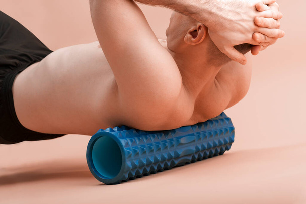 Спортивный человек с помощью миофасциального ролика для мышц и фасции, растягивающихся назад. Красивый человек делает упражнения с пенопластом - Фото, изображение