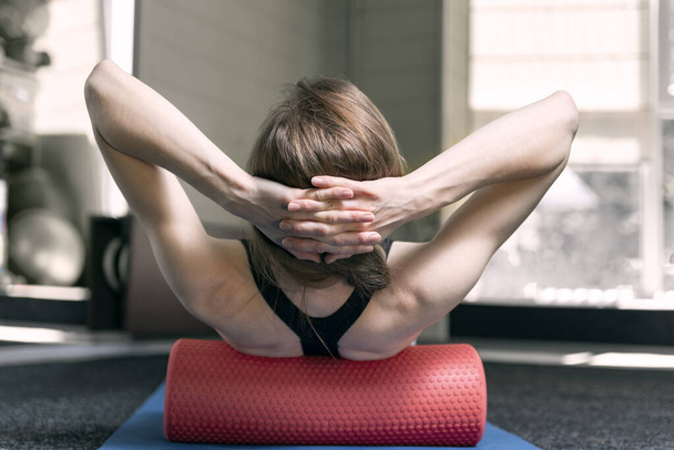 Девушка со спортивным телосложением делает миофасциальное освобождение спины с помощью пенопласта. Ролик для физиотерапии - Фото, изображение