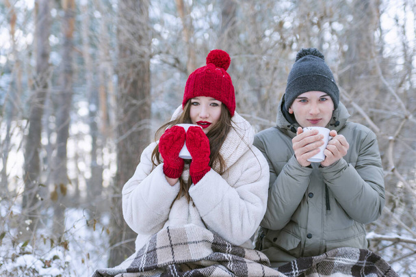 Young couple had picnic in forest in winter. Lovers wrapped themselves in blanket and drink tea. - Fotografie, Obrázek