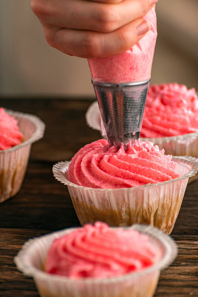 Female hand decorates freshly baked cupcakes with cream. Cakes with berry cream. Vertical frame - Valokuva, kuva