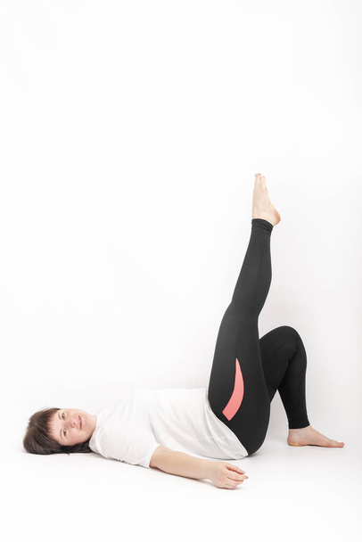 Curvy woman in sportswear holding doing exercise. Girl lies on back with her leg raised on white background. Vertical frame. - Foto, Imagem