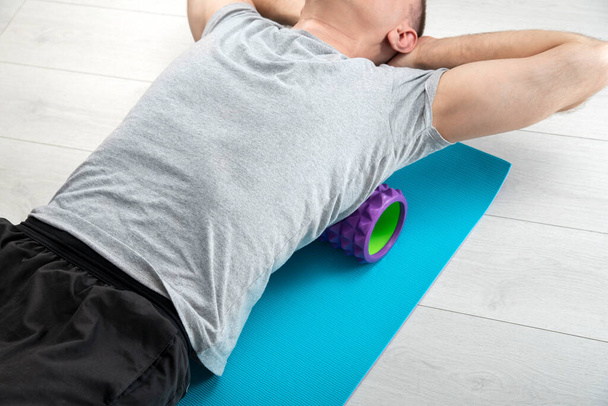 Man lies on the myofascial roller. Man performs myofascial release of hyper-movable back muscles with massage roller - Φωτογραφία, εικόνα