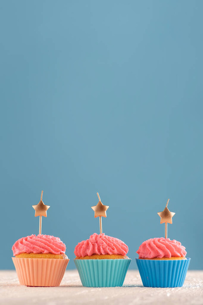 Postal festiva con tres magdalenas rosas y velas en forma de estrellas sobre fondo azul. Copiar espacio. Marco vertical. - Foto, imagen