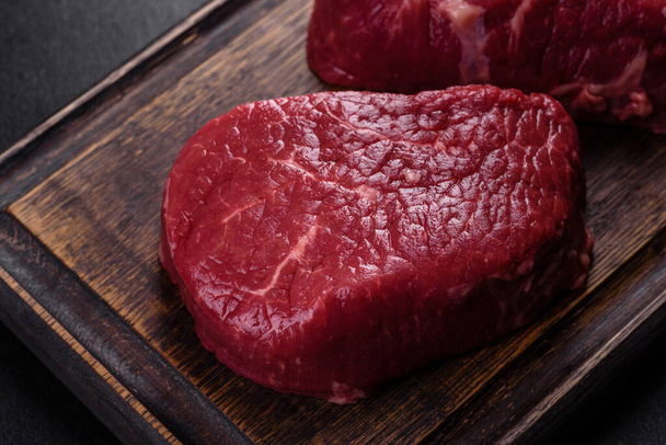 Raw beef steaks on a cutting board with spices on a stone background - Photo, image