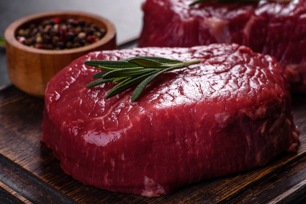 Raw beef steaks on a cutting board with spices on a stone background - Photo, Image