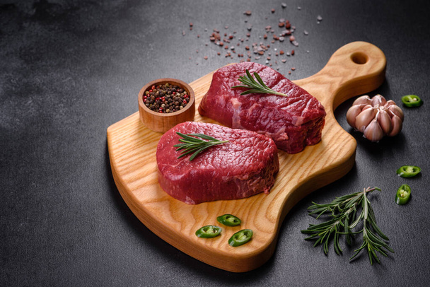Rauwe biefstuk op een snijplank met specerijen op een stenen ondergrond - Foto, afbeelding