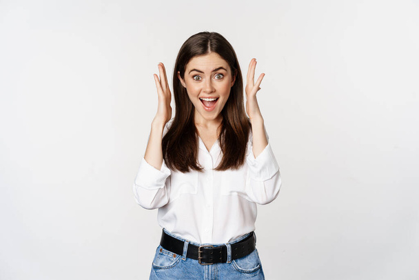 Excited young adult woman reacting to win, surprise news, screaming and cheering, triumphing, achieve goal and celebrating, standing over white background - Φωτογραφία, εικόνα
