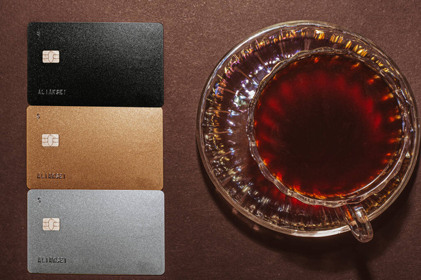 Top view of a cup of coffee and black, gold, silver, credit card, isolate on black - Zdjęcie, obraz