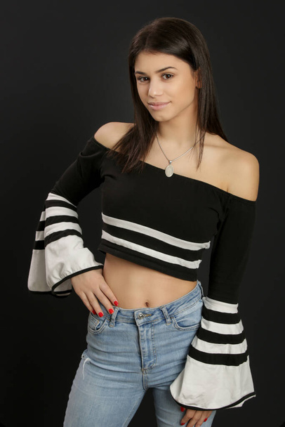 Portrait of attractive young brunette wearing cold shoulder top on black background - Zdjęcie, obraz