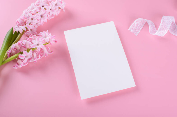 Leere Hochzeitseinladungskarten-Attrappe auf rosa Hintergrund mit Hyazinthenblüten und weißem Band, feminine Blog-flache Lage, Draufsicht. Minimalistisches 5x7-Mockup-Verhältnis, ähnlich A6, A5 - Foto, Bild