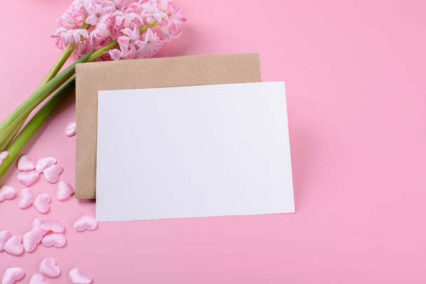 Tarjeta de papelería de invitación a la boda en blanco maqueta con sobre sobre sobre fondo rosa con flores de jacinto y corazón rosa - Foto, Imagen