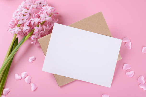 Tarjeta de papelería de invitación a la boda en blanco maqueta con sobre sobre sobre fondo rosa con flores de jacinto y corazón rosa - Foto, Imagen