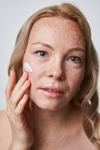 Woman isolated on white studio background applying daily moisturizing face cream - Zdjęcie, obraz