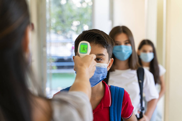 Teacher checking temperature of students with face mask for pandemic while children go back to school - Photo, image
